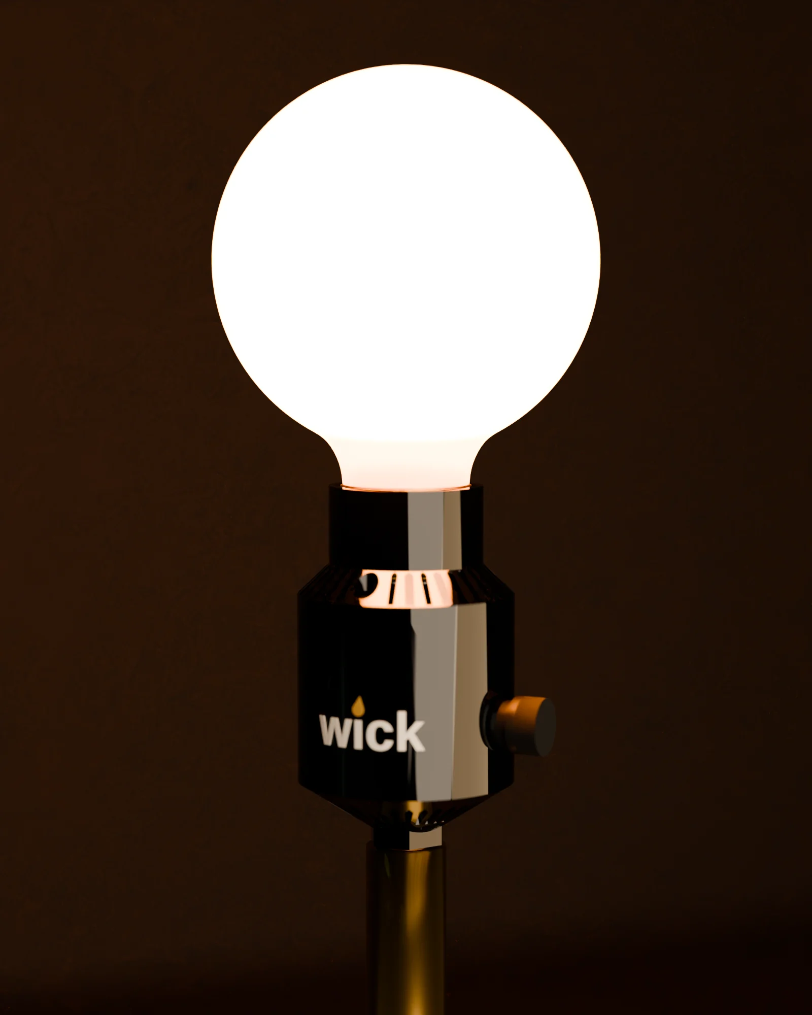 A walnut and brass table lamp with a bare globe bulb on a Gloss black wick in the cone shape, its louvers lit from within