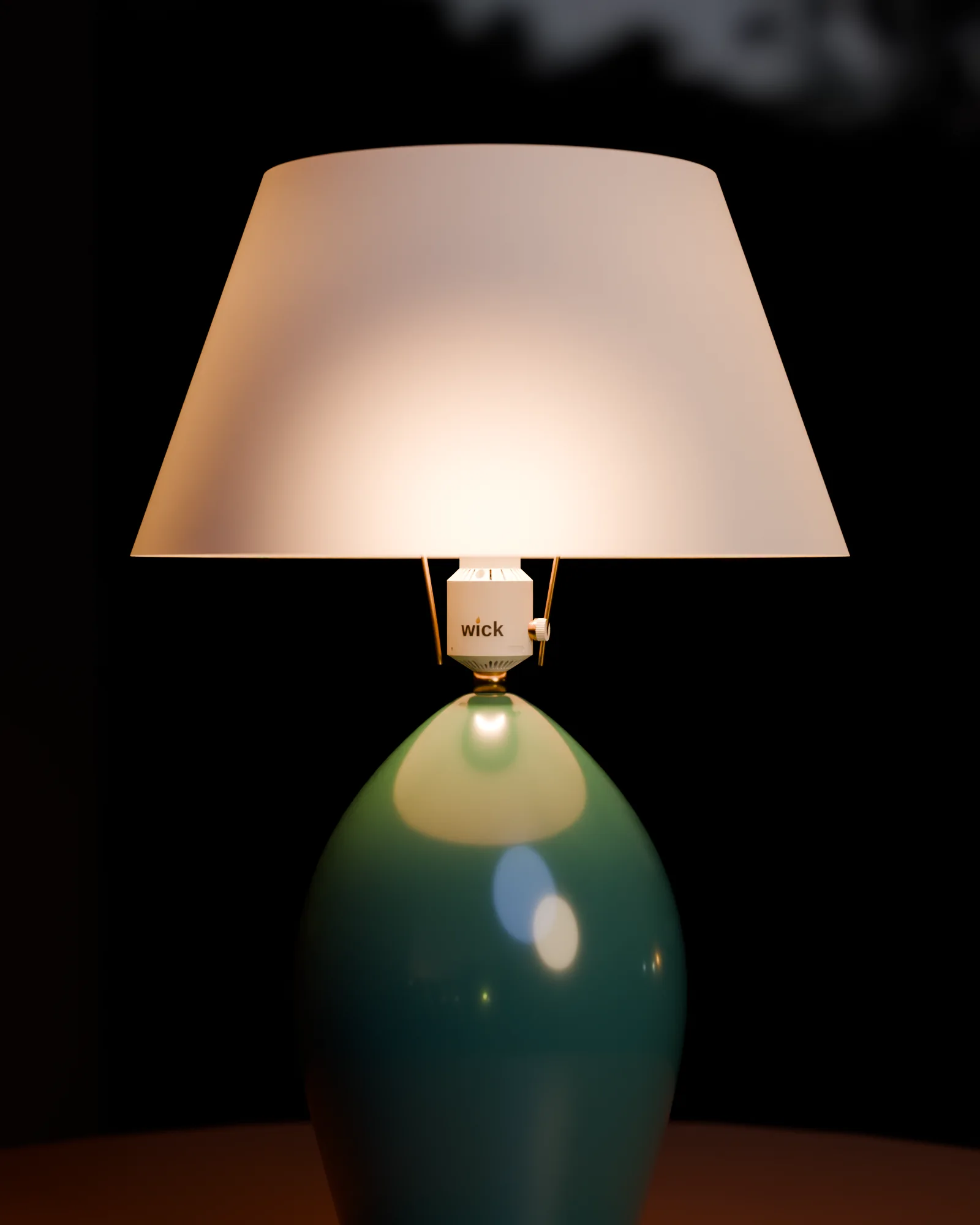 A green ceramic table lamp with a white shade, a white wick socket on the harp under the shade